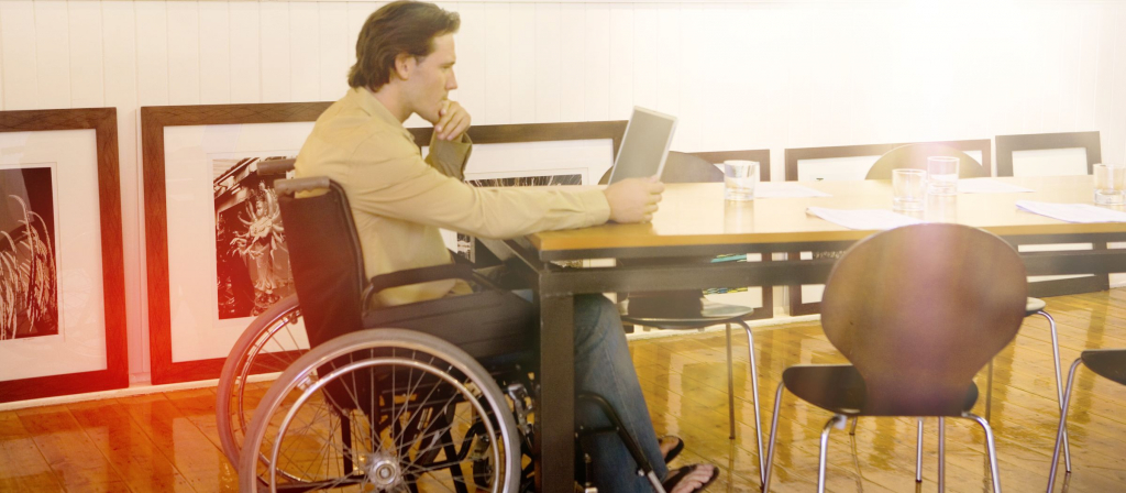 Das Bild zegt einen Mann im Rollstuhl, der an einem Tisch sitzt und sich am PC über eine Berufsunfähigkeitsversicherung informiert.