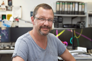 Ein Bild von Karsten Lehmkuhl in einem grauen T-Shirt in seinem Büro an der Uni Bremen.