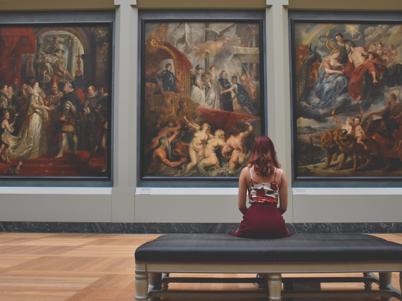 Eine junge Frau vor eine Gemäldewand in einem Museum