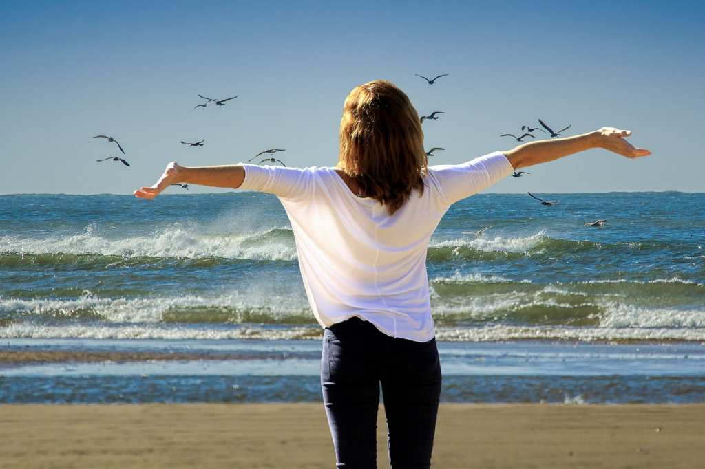 Eine Frau steht am Strand und atmet frische Meerluft ein